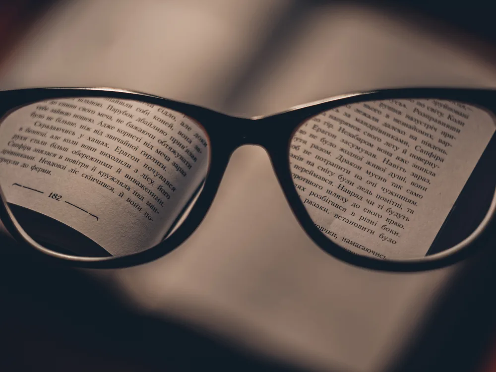 Eyeglasses held up against a scene, the view sharpened through the lenses